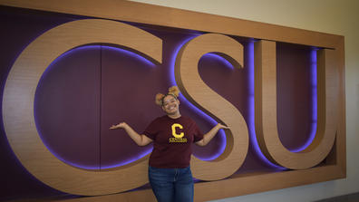 a student stands in front of a large wall sign that says C-S-U for Central State University