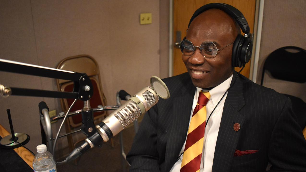 Morakinyo A.O. Kuti with a maroon and gold striped tie using broadcast equipment for a podcast