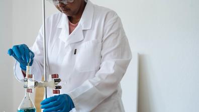 A Black scientist works in a lab with a white healthcare coat
