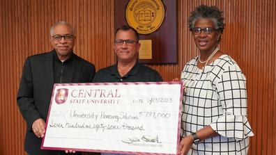 three people hold a large decorative check for University Housing Solutions' donation to Central State University in the amount of $787,000