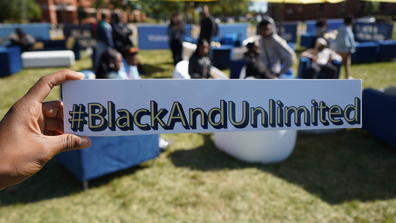 An African American holds a sign with the hashtag Black and Unlimited as part of Walmart's tour of HBCUs
