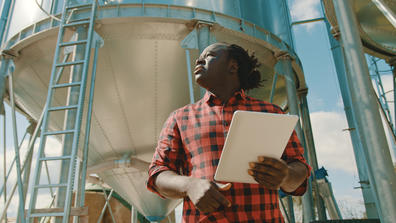 an African American farmer holding a tablet outside a water tower