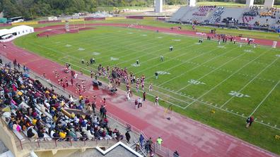 an aerial view of the Marauder Athletics football team on the field with a large crowd cheering them on