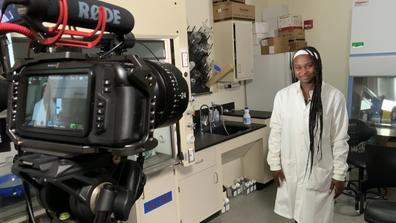 Alexis Draper wearing a white lab coat in front of a camera recording a video
