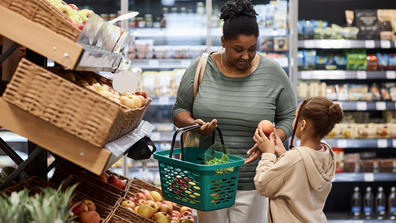 Portrait of real black woman shopping in supermarket with little daughter and buying fresh vegetables