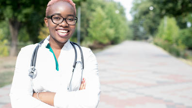 Portrait of a young black girl, a doctor in a white coat, with a phonendoscope. Smiling looking at camera, outdoor
