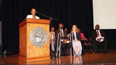 speaker latoya turner speaks at a podium with leadership looking on nearby at a freshman convocation in the paul robeson cultural and performing arts center