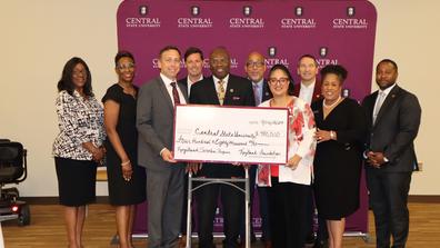 a large group of people stands in front of a central state university backdrop with president dr. morakinyo kuti and keybank representatives holding a large check