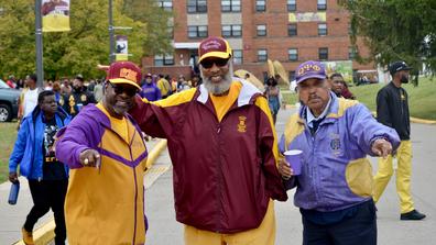 three men in maroon and gold attire attend homecoming tailgating