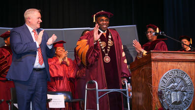 central state university president dr. morakinyo a.o. kuti waves from the stage while ohio department of higher education chancellor mike duffy looks on