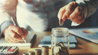 person saving money hand holding coins putting in jug glass