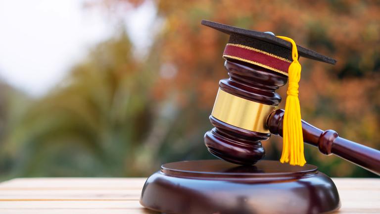 A judge's gavel with a tiny graduation cap on top