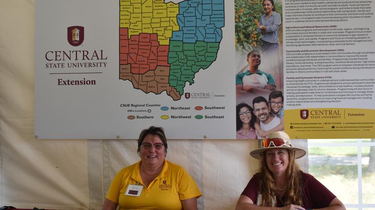 two representatives of Central State University Extension sit at a table with a large map of the state of Ohio showing the various regions of Extension offices