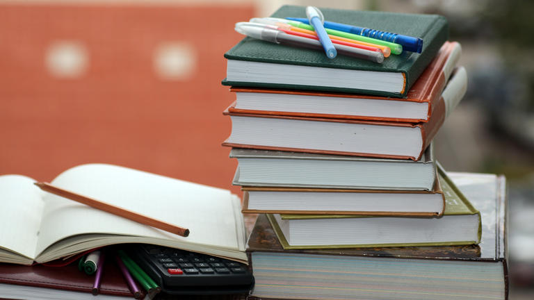 a stack of college textbooks, pens, notebooks, and a calculator