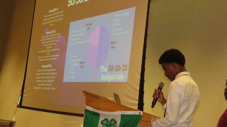 youth presenter at a podium with a display of a presentation about budgeting