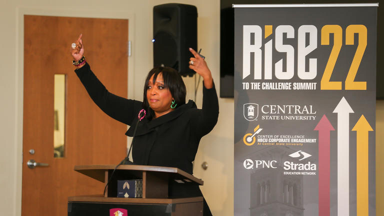 a speaker at RISE to the Challenge holds her hands up in the air
