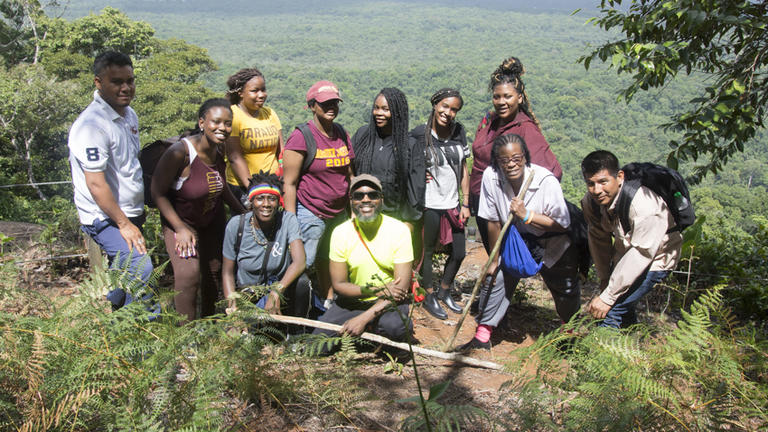 A student group poses in front of promontory vista of a rainforest in Guyana.