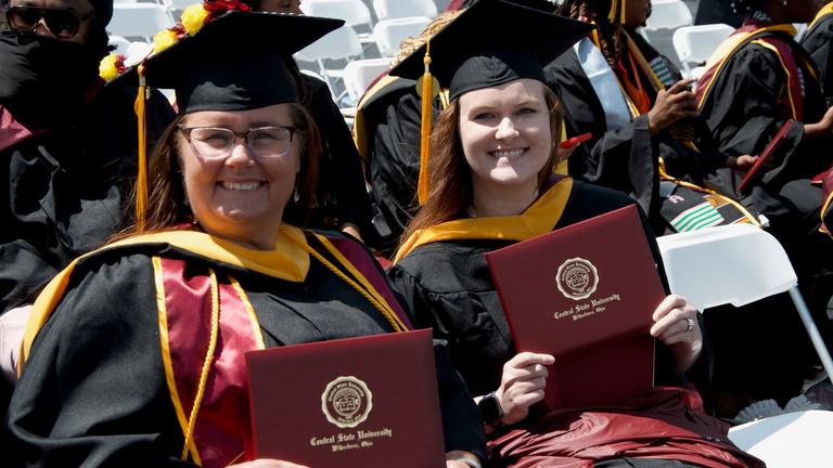 two central state university graduates hold their diplomas