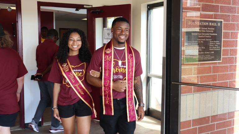 mister junior and miss junior wearing sashes outside a residence hall