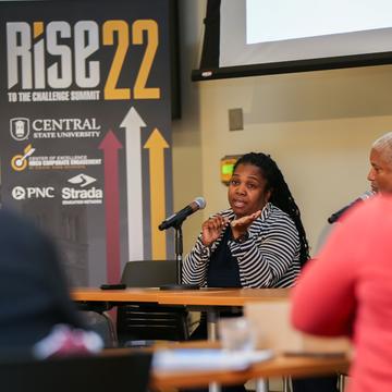 a panelist speaks during the rise 22 conference at central state university with a university-branded poster in the background as the audience listens in