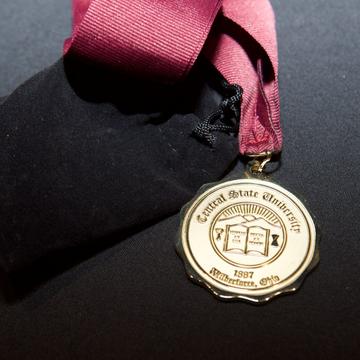 a gold medallion with the Central State University seal on a maroon landlord