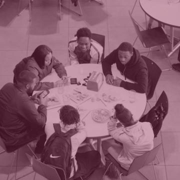 six students sit work together around a table in a bird's eye view with a maroon overlay