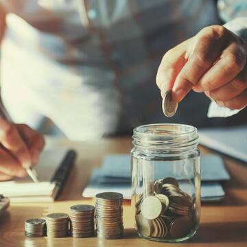 person saving money hand holding coins putting in jug glass