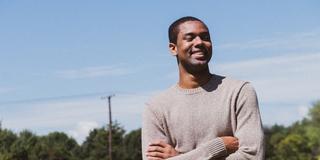 Black man crossing his arms and smiling in a field of sunflowers