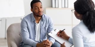 a behavioral health worker takes notes while speaking to a young Black man in an office setting