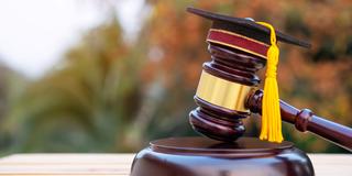 A judge's gavel with a tiny graduation cap on top