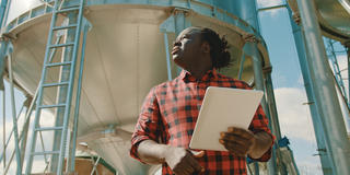 an African American farmer holding a tablet outside a water tower