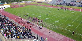 an aerial view of the Marauder Athletics football team on the field with a large crowd cheering them on