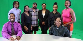 Students and Faculty standing at a news desk in front of a green screen