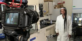 Alexis Draper wearing a white lab coat in front of a camera recording a video