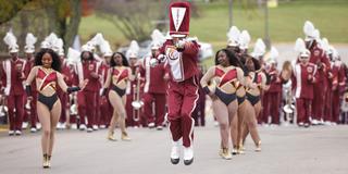 the invincible marching marauders from central state university. a person in front is jumping with feet off the ground and pointing straight ahead as the dance team and the rest of the marching band follows