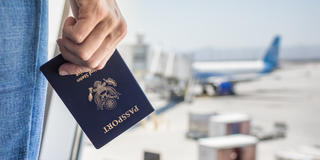 Hand holding passport facing airport window at boarding gate.