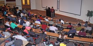 a professor stands at the front of a lecture hall with students seated in class