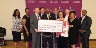 a large group of people stands in front of a central state university backdrop with president dr. morakinyo kuti and keybank representatives holding a large check