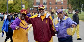 three men in maroon and gold attire attend homecoming tailgating