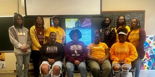 nine students and a professor in a central state university art classroom with a flyer for study abroad in paris on the screen behind them