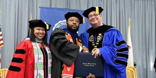 three people wearing regalia at a graduation ceremony with ramon moon in the center holding his diploma