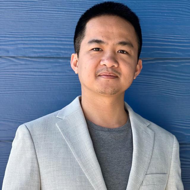 Phi Nguyen, a Nationwide intern, wears a gray suit jacket with a darker gray shirt in front of a sky blue background