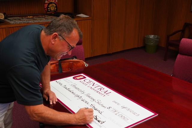 A man signs a large check for University Housing Solutions' gift of $787,000 to Central State University