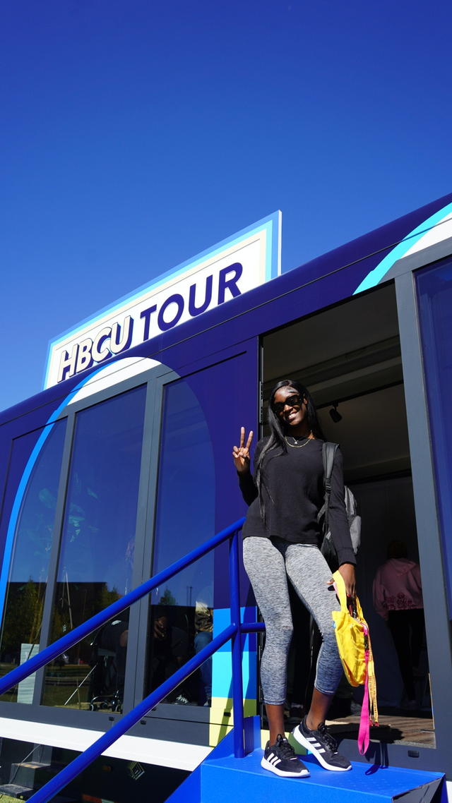 a student wearing a black coat and gray pants waves a peace sign outside the Walmart Black and Unlimited tour bus at Central State University, an HBCU in Wilberforce, Ohio