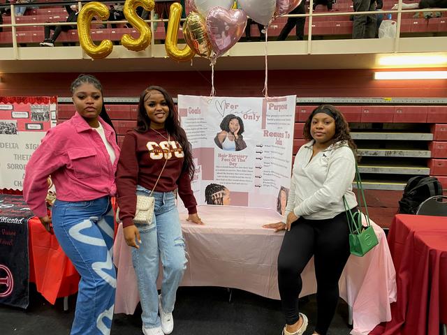 three Central State University students stand beside a display for the student organization For Curls Only during College Preview Day