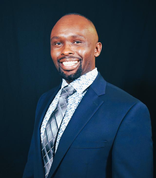 Central State University Food Safety Research Professor Robert Korir, Ph.D., in a dark blue suit with a spotted white shirt and striped tie in front of a darker blue wall