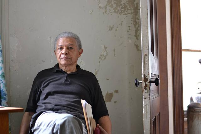 Charles Fox sits in an old building with books and papers in his left hand