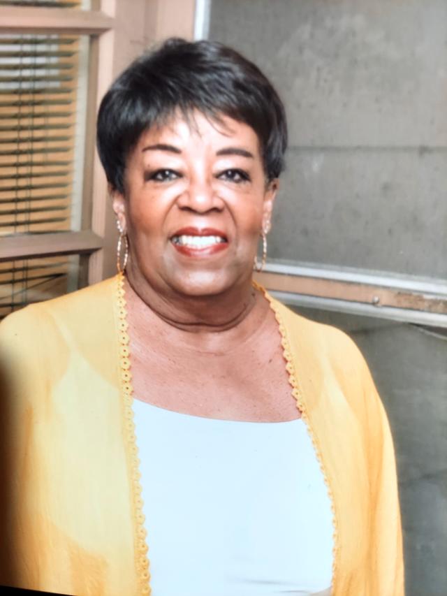 Ethel M Washington a Black woman with dark short hair wearing makeup, earrings and a yellow jacket over a white blouse