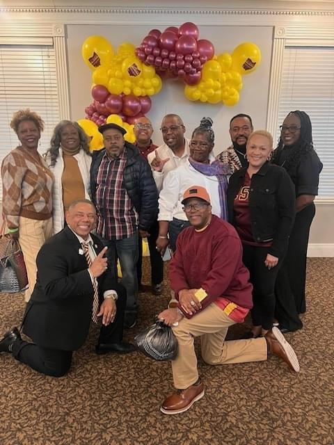 a large group of people stands in front of maroon and gold balloons