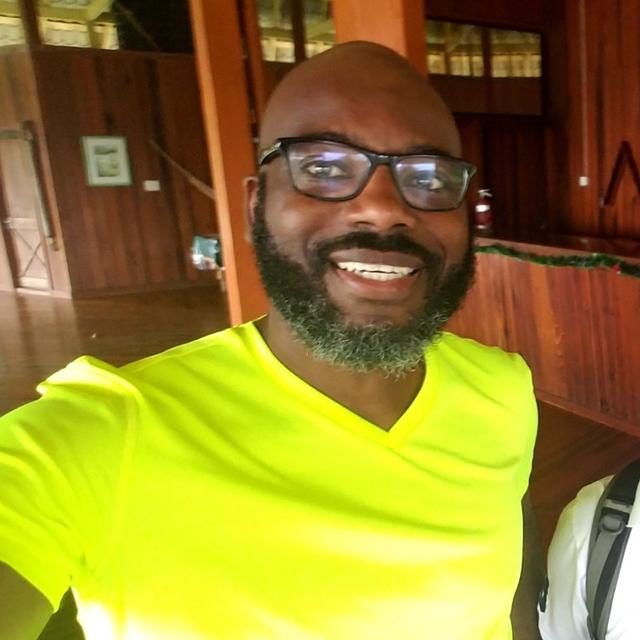 Dr. Geoffrey Giddings, a Black man with a beard wearing glasses in a yellow shirt 